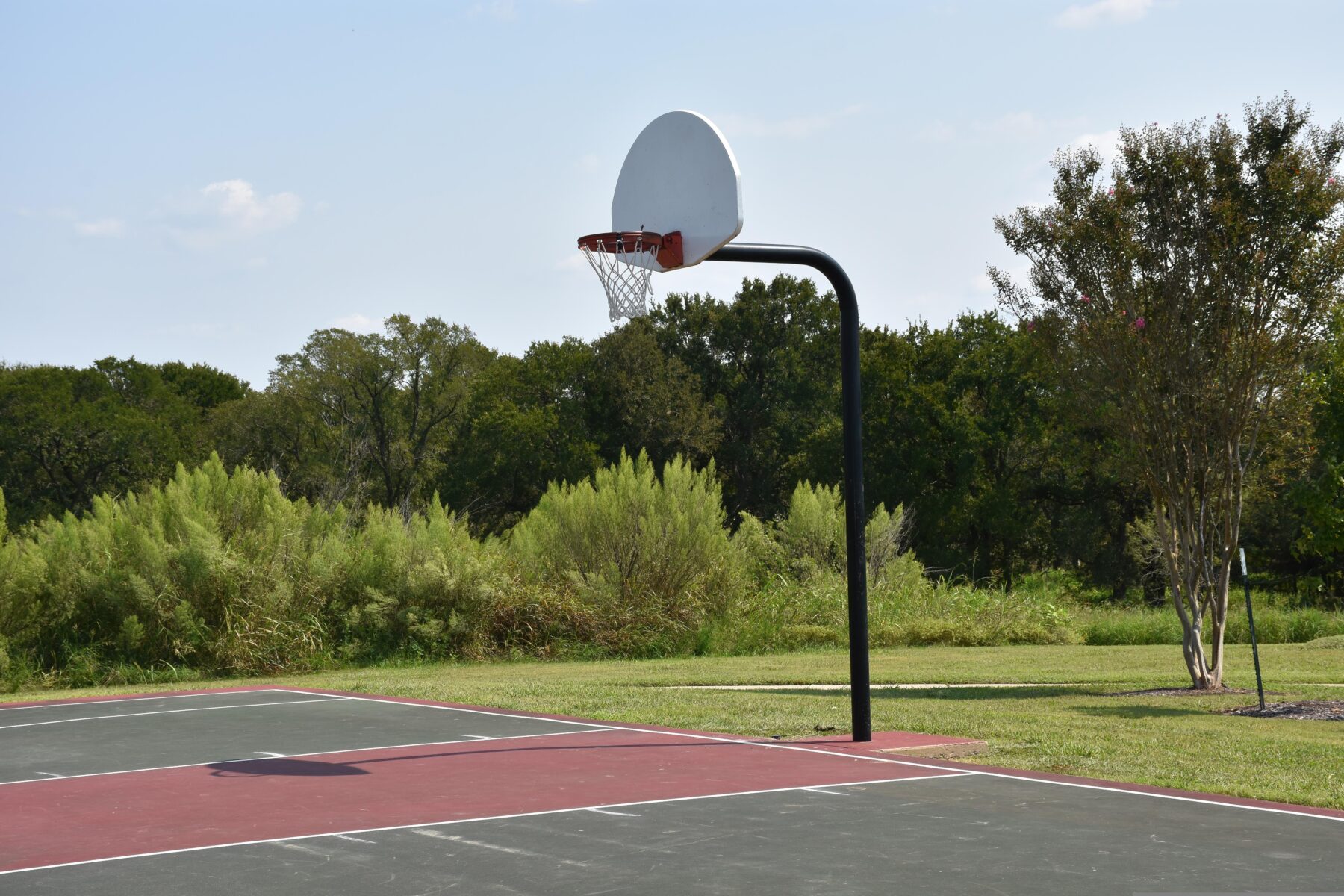 Outdoor asphalt basketball court in a tree-lined Des Moines park with clear skies